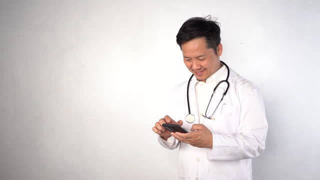 Horizontal banner of a young male doctor in a white coat smiling holding his smartphone with one hand using a medical app.
