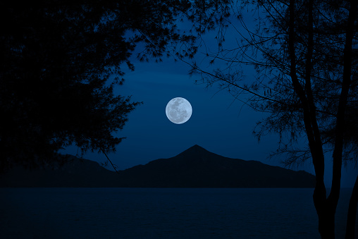 Full moon on sky over sea with mountain in the night.