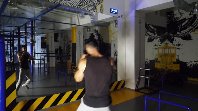 Strong sporty man practicing shadow boxing at sport club. Young muscular athlete demonstrating punches the air at modern gym. Male kickboxer training at fitness centre. Concept of healthy lifestyle