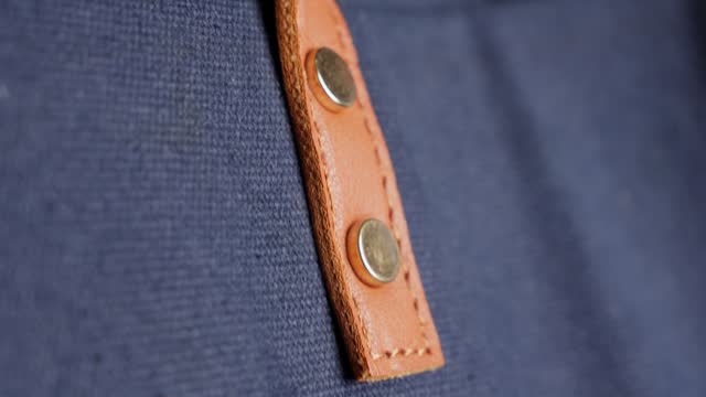 Close-up of a tan leather belt with metal rivets on blue cotton fabric, detailing textures