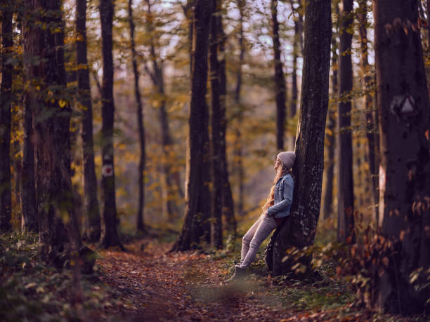 Young woman leaning on a tree while spending an autumn day in the forest. Copy space. Photographed in medium format.