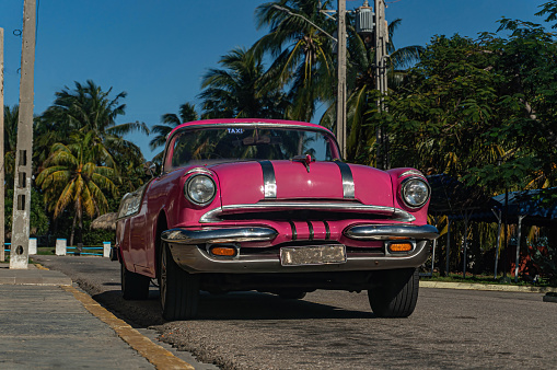Bright pink retro convertible with palm trees on the streets of Varadero on Cuba. Low angle