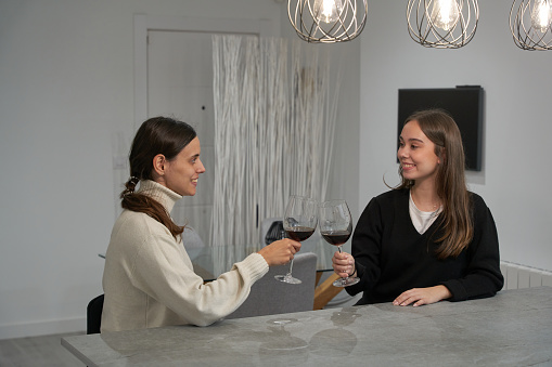 Two girls talking and having a cup of wine in a beautiful minimalist white kitchen