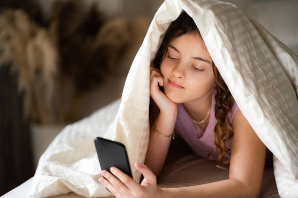 adolescente deitada na cama e mandando mensagens no celular - one teenage girl only on the phone bed lying on front - fotografias e filmes do acervo