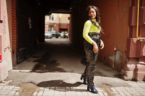 Portrait of young beautiful african american fashion model woman, wear in green top and black shiny wet look pants, posed against arch tonnel.