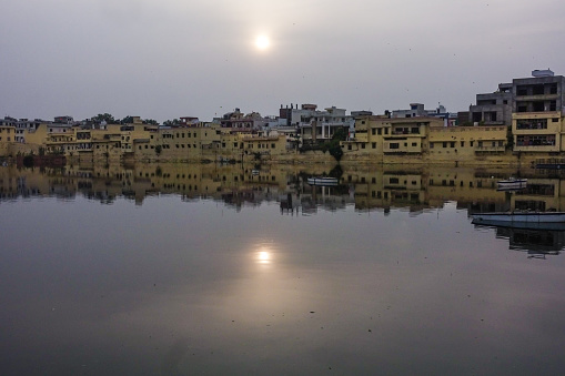 Sun shining over the residential buildings with its reflections on the water surrounding Talkatora Lake in Jaipur, Rajasthan