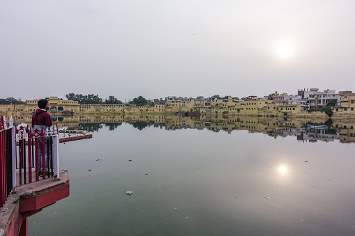 Man viewing the scenery of the sun shining over the residential buildings with its reflections on the water surrounding Talkatora Lake from a terrace in Jaipur, Rajasthan