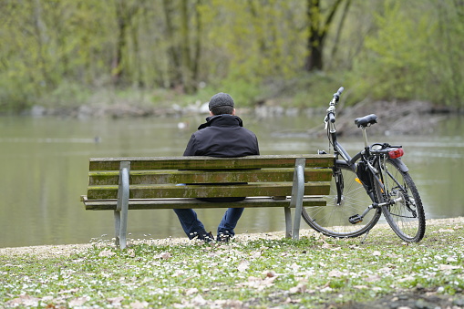 Legnano, Italy - April 01, 2024: man sitting on the bench in front of a pond