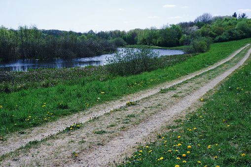 View of dirt road in countryside near the pond. Rural spring landscape with empty countryside dirt road.