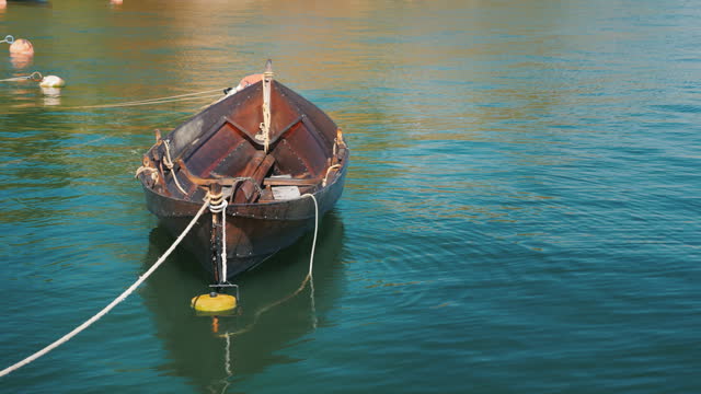 A fishing boat is moored at the shore. Slowly swinging on a wave in a clear summer day