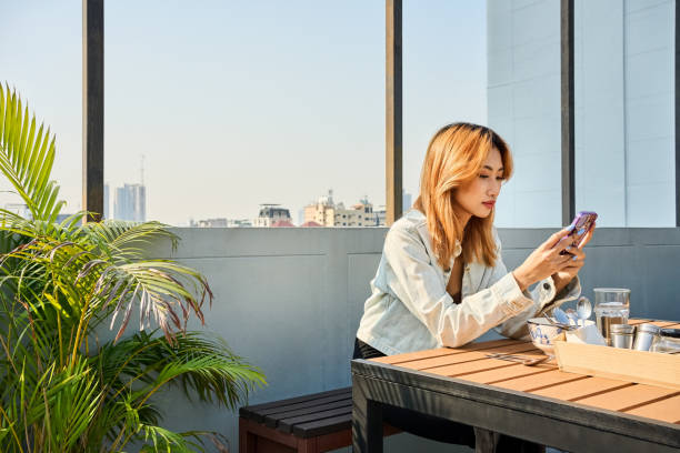 istock Asian woman using mobile phone while sitting at rooftop cafe 2132200272