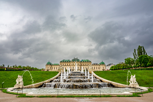 Belvedere Baroque palace in Vienna seen from the public gardens with fountains and dark clouds above.