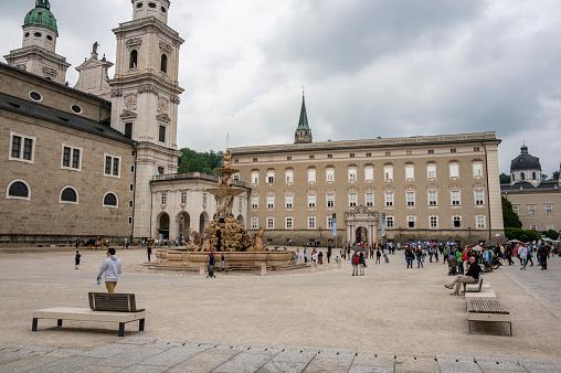 Residenzplatz square with Residenz fountain in the Old Town of Salzburg, Austria during an overcast springtime day with tourist walking on the square.