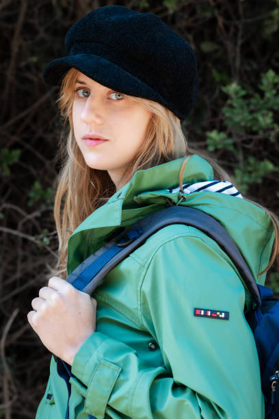 istock Blonde girl with a dark hat, warm jacket, and backpack looking at the camera 2132205514