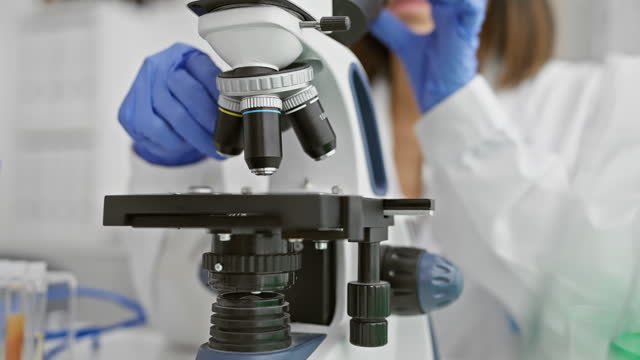 Scientist in lab coat using a microscope for medical research in laboratory environment.