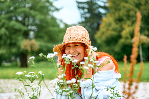 Senior woman crouching on a meadow and enjoying while looking at flowers.