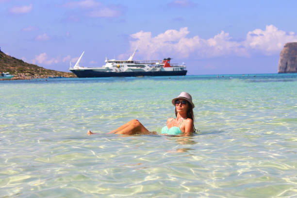 woman in a hat sits in the water in front of a cruise ship
