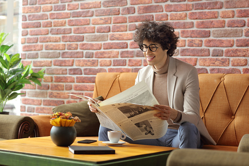 Businesswoman reading newspaper in cafe, Young female sitting at coffee shop table reading a newspaper.