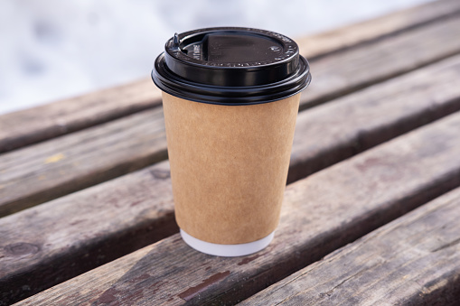 Paper cup with coffee on wooden bench on snow background.
