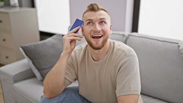 Handsome bearded man holding credit card contemplating shopping at home