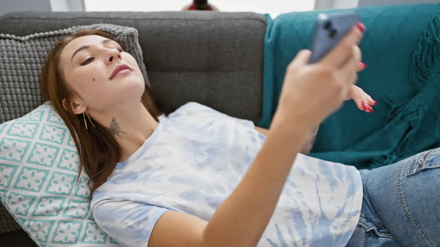 A relaxed young woman lounges on a sofa using her smartphone in a cozy home interior.