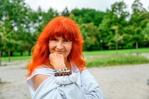 Portrait of a senior woman with red dyed hair in a public park.