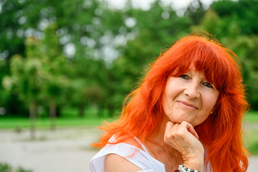 Portrait of a senior woman with red dyed hair in a public park.