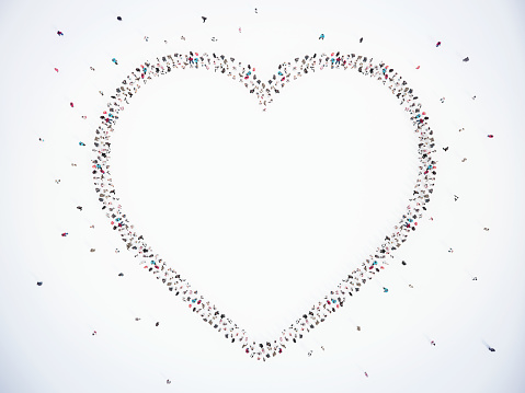 A large, diverse group of individuals stand together, creating a massive heart formation against a stark, white backdrop, symbolizing unity, love, and community.