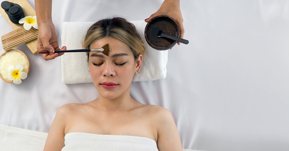 Young asian woman with nutrient facial, getting facial care by beautician at spa salon, Top View. Face peeling mask, spa beauty treatment, skincare. Spa concept