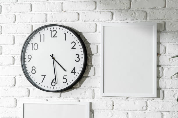 minimalist white wall decor featuring a clock and blank photo frames - customisable fotografías e imágenes de stock