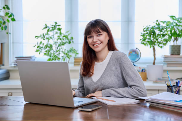 istock Young female college student studying at home using laptop, looking at camera 2132306613