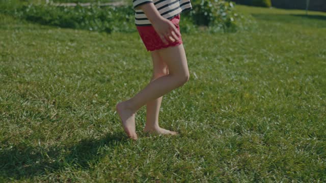 Little baby girl walking barefoot on green grass in summer close-up slow motion