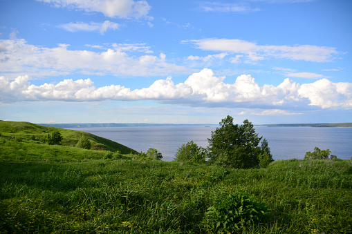 a grassy hill with a lake in the background and a blue sky with clouds