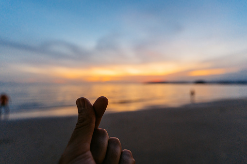 Young man making a finger heart on the Ao Nang beach at sunset in Thailand. His POV.
