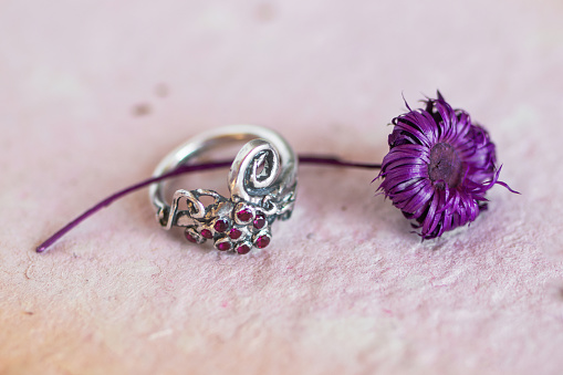 Silver ring with pink stones on a pink background with dry purple flower. Handcraft precious item. Jewelry accessories.