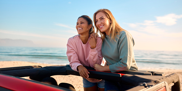 Two Women On Vacation In Car Driving On Road Trip Adventure To Beach Standing Up Through Roof