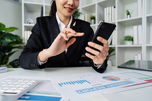 business woman using smartphone while working on laptop, synchronize data between computer and gadget in office, use corporate devices and business application.