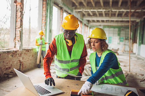 Male and female construction workers with laptop and blueprints at a building site