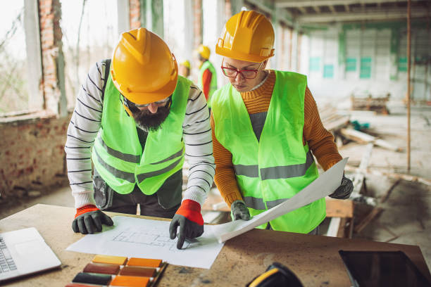 istock Two workers in hard hats and reflective vests review plans on a construction site 2132488296