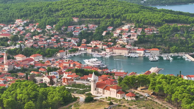 AERIAL: Quaint town of Hvar with marina nestled between greenery and sea.