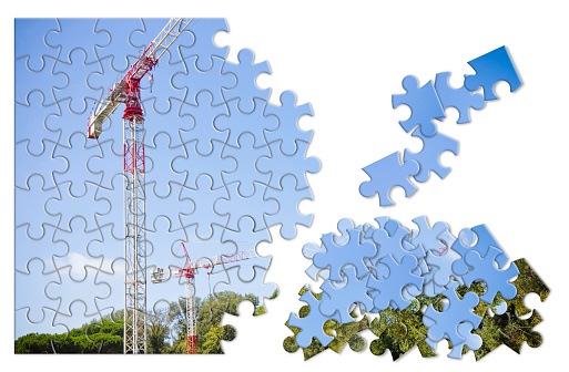 Metal tower crane, colored in white and red, against a blue background - solution concept in jigsaw puzzle shape