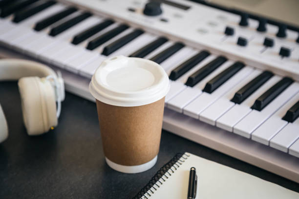 istock Musician workplace table with paper cup and white piano keyboard. 2132569213