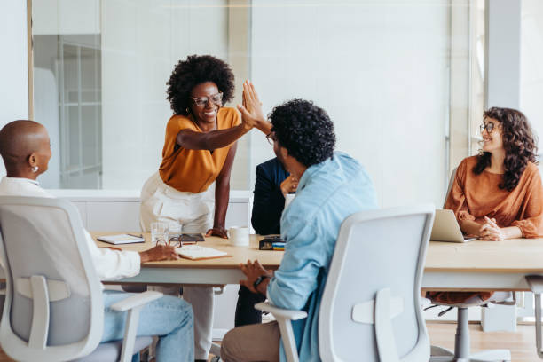 Business people celebrating a successful project with a high five in a boardroom. Business men and women showing teamwork, collaboration, and creativity in a diverse workplace environment.