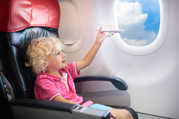 Child in airplane. Kid in air plane sitting in window seat. Flight entertainment for kids. Traveling with young children. Kids fly and travel. Family summer vacation. Little boy with toy in airplane.