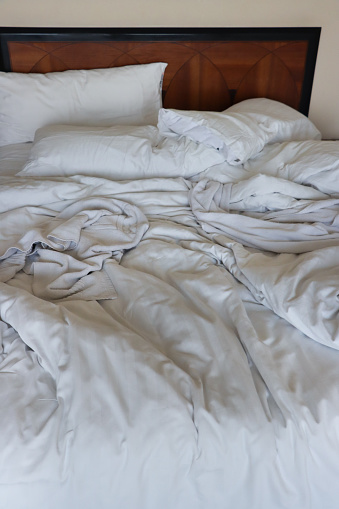 Stock photo showing close-up view of unmade double bed with crumpled, white bedding.