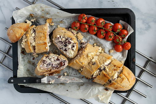 Delicious filled Baguette with feta cheese, herbs and kalamata olives. Served ready to eat on a baking sheet with roasted tomatoes.