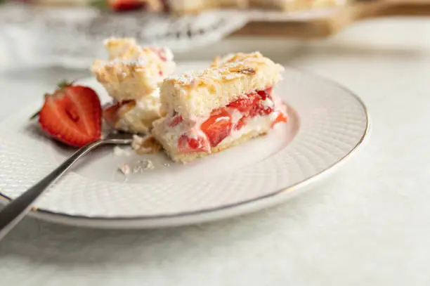 Piece of strawberry cake with chopped strawberries and whipped cream filling on a plate. Closeup