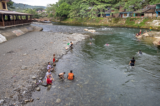 Bukit Lawang, Sumatra, Indonesia - January 19th 2024:  People washing both clothes and themselves in the river in the middle of the village