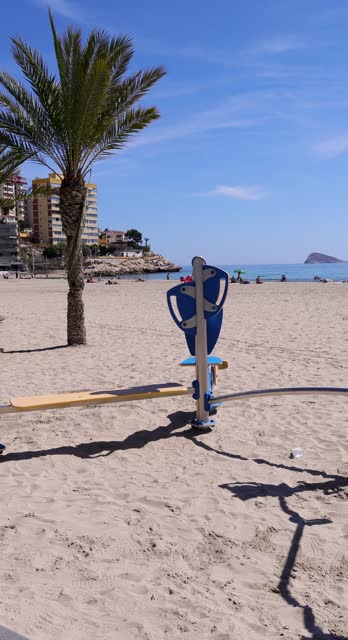 Footage of the town of Benidorm in Spain in the summer time showing the beach known locally as Playa de Finestrat with a children's playground on the sandy beach