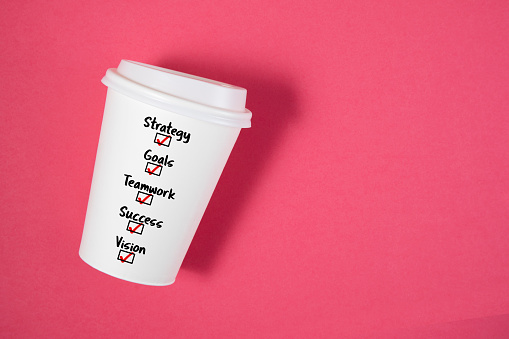 Conceptual shot with paper coffee cup and business related words; strategy, goals, teamwork, success and vision as a choice on it on pink background
